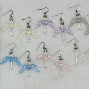 Puede incluir: Diez pares de pendientes de alas de &aacute;ngel en varios colores iridiscentes, incluyendo blanco, rosa, morado y azul. Los pendientes est&aacute;n hechos con peque&ntilde;as cuentas y tienen un dise&ntilde;o delicado y femenino.