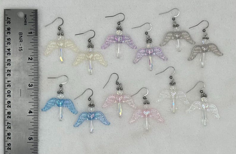 Puede incluir: Diez pares de pendientes de alas de &aacute;ngel en varios colores iridiscentes, incluyendo blanco, rosa, morado y azul. Los pendientes est&aacute;n hechos con peque&ntilde;as cuentas y tienen un dise&ntilde;o delicado y femenino.