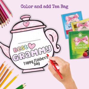 May include: A printable coloring page of a teapot with the words "Best Grammy Happy Mother's Day" on it. The teapot is outlined in black and has a pink heart on the lid. There are also three tea bags with pink bows on them.