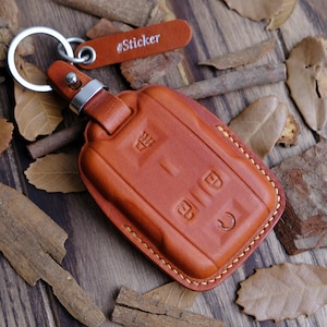 Könnte beinhalten: Ein brauner Leder-Schlüsselanhänger mit einem silbernen Schlüsselring und einem genähten Rand. Der Schlüsselanhänger hat ein #Sticker-Etikett.