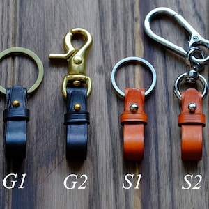 May include: Four leather keychains with different styles of clasps. Two keychains are black leather with gold clasps, labelled G1 and G2. Two keychains are orange leather with silver clasps, labelled S1 and S2.