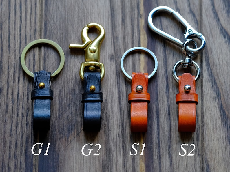 May include: Four leather keychains with different styles of clasps. Two keychains are black leather with gold clasps, labelled G1 and G2. Two keychains are orange leather with silver clasps, labelled S1 and S2.