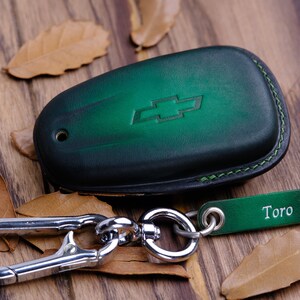 May include: Green leather key fob with a silver Chevrolet logo and a silver carabiner clip attached to a green leather tag that says "Toro".