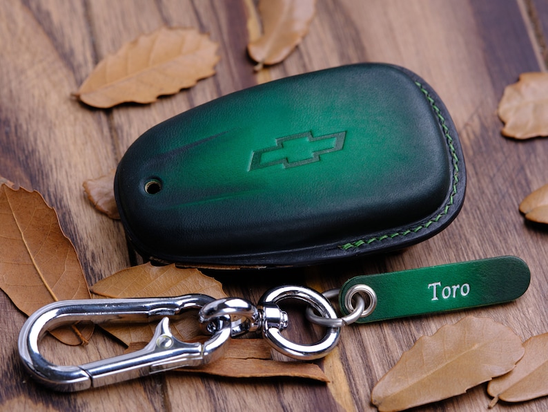 May include: Green leather key fob with a silver Chevrolet logo and a silver carabiner clip attached to a green leather tag that says "Toro".