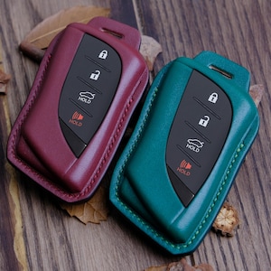 Puede incluir: Dos llaveros de cuero, uno burdeos y otro turquesa, con una llave de coche en el interior. La llave tiene cuatro botones, dos botones de bloqueo, un botón de retención y un botón de pánico.