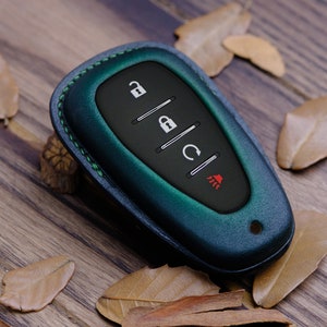 May include: A dark green leather key fob with a black keyless entry remote. The remote has four buttons: unlock, lock, boot release, and panic.