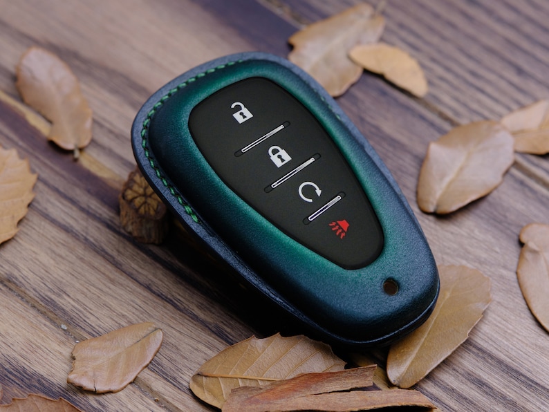 May include: A dark green leather key fob with a black keyless entry remote. The remote has four buttons: unlock, lock, boot release, and panic.
