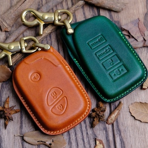 Puede incluir: Dos fundas de llaves de cuero, una marrón y otra verde, con llaveros dorados. La funda marrón tiene dos botones y la funda verde tiene cuatro botones.