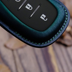 May include: A dark green leather key fob with a black remote control. The fob has green stitching detail around the edge.