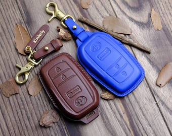May include: Two leather key covers for car keys. One is brown and the other is blue. Both have the Toyota logo on them. The brown key cover has the text "Kimberly" on the keychain.