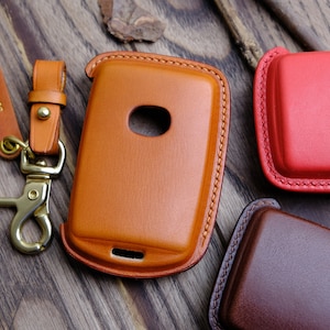 May include: Three leather key fobs in different colors: brown, red, and dark brown. The brown key fob has a small hole for a key and a metal clasp with a tag that says "Serena".