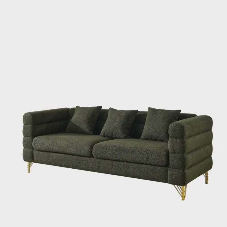 May include: A dark green sofa with three matching throw pillows. The sofa has a textured fabric and a unique arm design. The legs are gold-colored. A modern piece of furniture for a living room or lounge area.