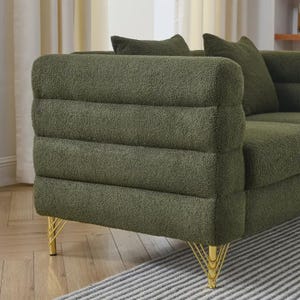 May include: Olive green sofa with a textured, ribbed design on the armrest. The sofa has gold-colored metal legs. Two matching throw pillows are visible. The sofa is placed on a striped rug.