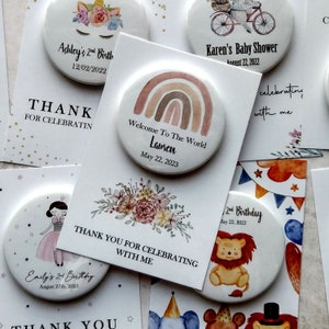 May include: Assortment of colorful round buttons with various designs and text. The buttons feature illustrations of a unicorn, a rainbow, a lion, a floral bouquet, and a girl in a dress. The text on the buttons includes names, dates, and phrases like "Welcome to the World", "2nd Birthday", and "Thank You for Celebrating with Me".