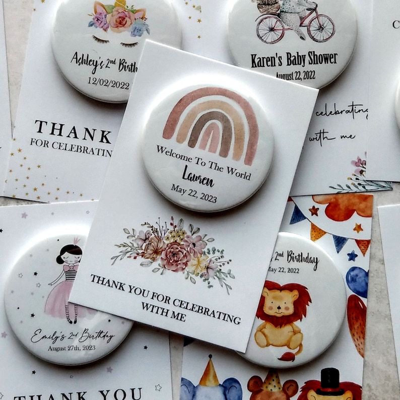 May include: Assortment of colorful round buttons with various designs and text. The buttons feature illustrations of a unicorn, a rainbow, a lion, a floral bouquet, and a girl in a dress. The text on the buttons includes names, dates, and phrases like "Welcome to the World", "2nd Birthday", and "Thank You for Celebrating with Me".