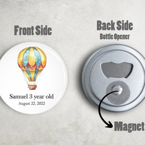 May include: A round magnet with a hot air balloon design. The front side features a yellow and blue hot air balloon with red accents. The text "Samuel 3 year old August 22, 2022" is printed below the balloon. The back side is a bottle opener.