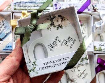 May include: A white ceramic mug in a gift box, decorated with floral accents and a green ribbon. The mug is personalized with the names "Alyssa & Toby" and the date "10.10.2025". The box includes the text "THANK YOU FOR CELEBRATING WITH".
