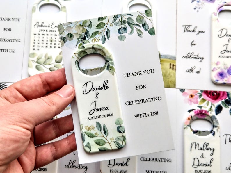 K&ouml;nnte beinhalten: Wei&szlig;er Flaschen&ouml;ffner mit botanischem Design und den Namen "Danielle & Jenica" und dem Datum "03. August 2026". Auf der Karte steht "Danke, dass Sie mit uns feiern!" Hochzeitsgeschenke.