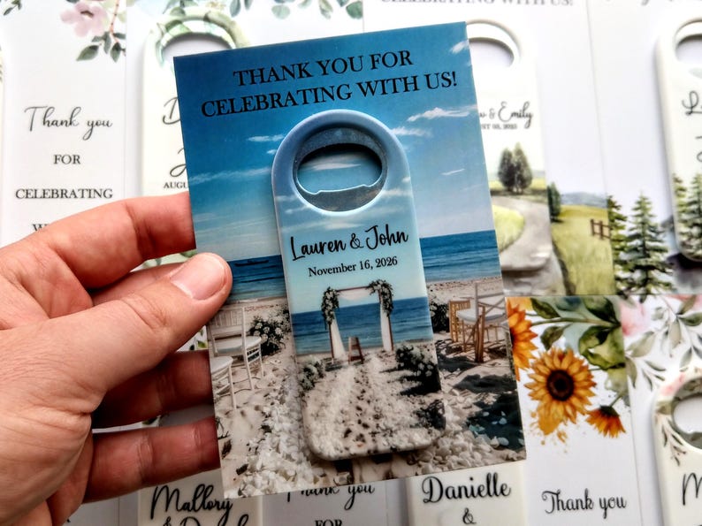 K&ouml;nnte beinhalten: Ein Flaschen&ouml;ffner mit Strandhintergrund, mit dem Text "Thank you for celebrating with us!" und den Namen "Lauren & John" mit dem Datum "November 16, 2026". Weitere Karten mit Blumen- und Landschaftsmotiven sind sichtbar.