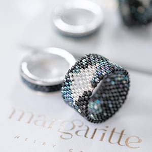 Könnte beinhalten: Nahaufnahme von Perlenringen in Schwarz, Weiß und Türkis. Die Ringe liegen auf einer weißen Oberfläche, auf der der goldene Text "margariitte" zu sehen ist. Die Ringe haben ein geometrisches Muster.