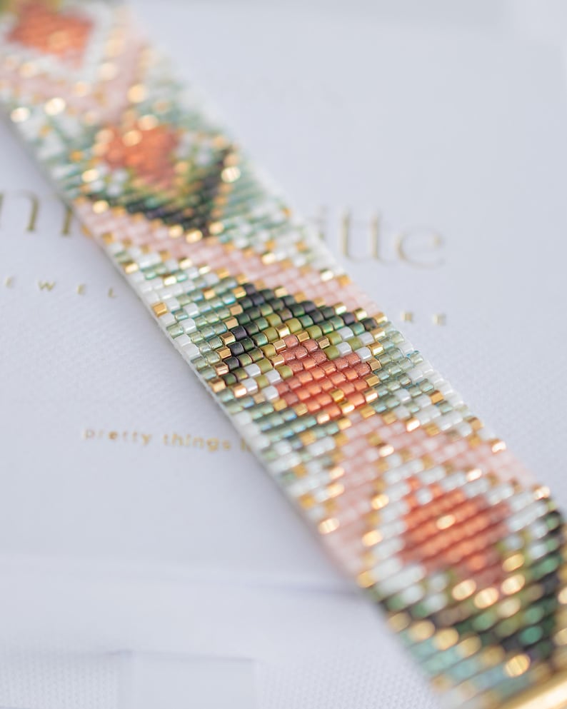 Puede incluir: Primer plano de una pulsera de cuentas con un patr&oacute;n floral. La pulsera presenta un dise&ntilde;o repetido de cuentas melocot&oacute;n, verdes y blancas, acentuadas con cuentas doradas. La pulsera est&aacute; sobre una superficie blanca con el texto "pretty things".