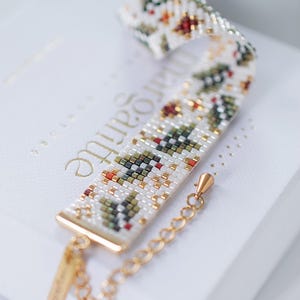 Könnte beinhalten: Ein Armband mit Perlen auf weißem Hintergrund. Das Armband hat ein sich wiederholendes Muster aus grünen, roten und goldenen Perlen. Das Armband ist etwa 18 cm lang und hat einen goldfarbenen Verschluss und eine Kette.