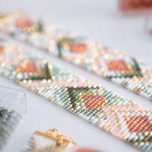 Puede incluir: Primer plano de dos pulseras de cuentas con un patr&oacute;n floral en tonos rosa, naranja, verde y blanco. Las pulseras tienen cierres dorados y est&aacute;n sobre un fondo blanco. Se ven cuentas de varios colores.
