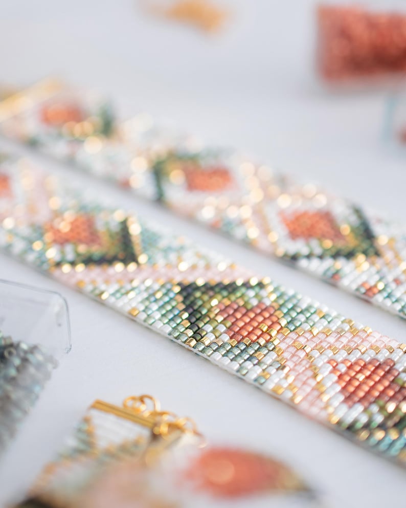 Puede incluir: Primer plano de dos pulseras de cuentas con un patr&oacute;n floral en tonos rosa, naranja, verde y blanco. Las pulseras tienen cierres dorados y est&aacute;n sobre un fondo blanco. Se ven cuentas de varios colores.