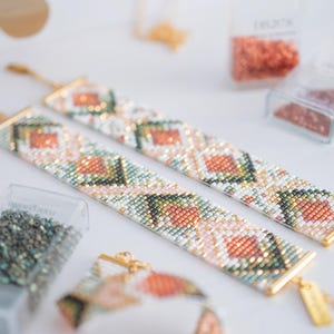 Puede incluir: Dos pulseras de cuentas con un patr&oacute;n geom&eacute;trico en tonos melocot&oacute;n, verde y blanco, con cierres y etiquetas doradas. Las pulseras est&aacute;n dispuestas sobre una superficie blanca, con recipientes de cuentas en el fondo.