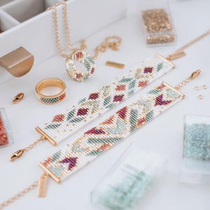 May include: A selection of handmade jewellery and craft supplies. Two beaded bracelets with floral patterns in white, red, and green are shown. A matching ring and necklace are also visible, along with containers of beads and jewellery-making tools.