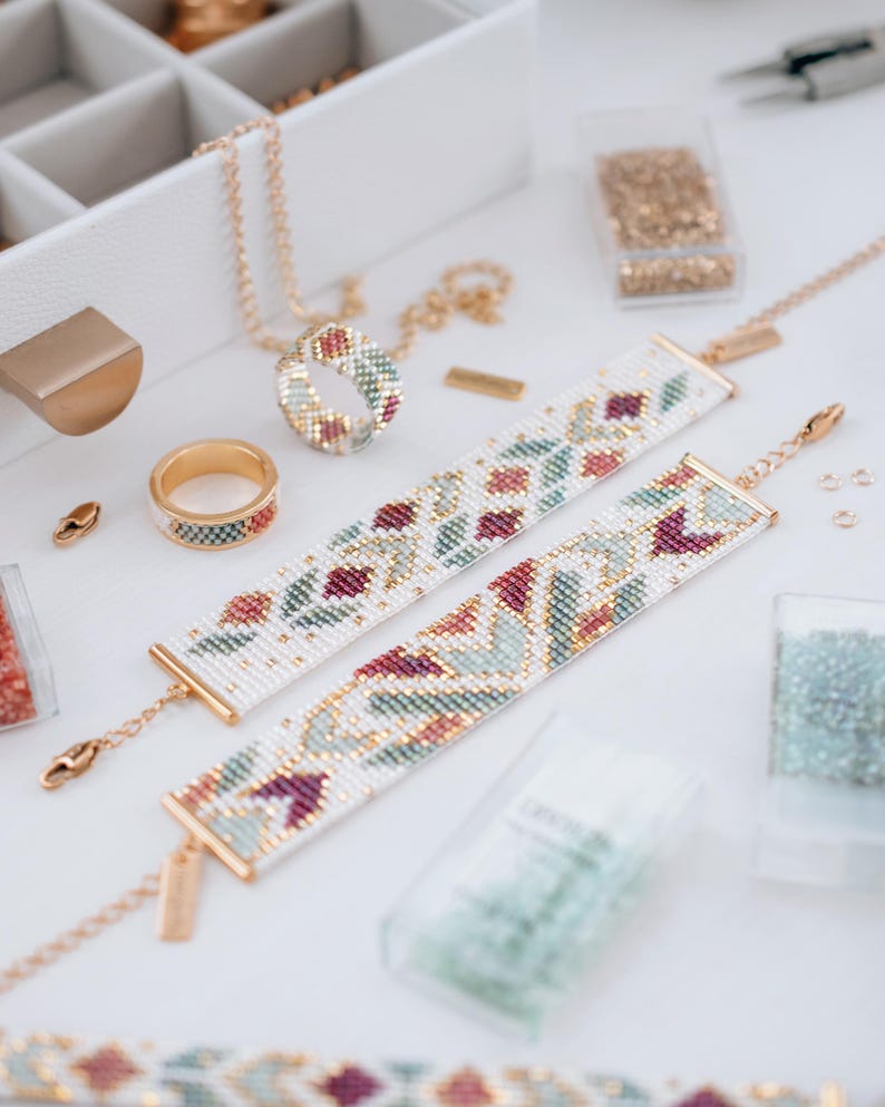 May include: A selection of handmade jewellery and craft supplies. Two beaded bracelets with floral patterns in white, red, and green are shown. A matching ring and necklace are also visible, along with containers of beads and jewellery-making tools.