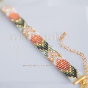 May include: A beaded bracelet with a floral pattern in shades of peach, green, gold, and white. The bracelet is attached to a gold chain and clasp. The text "pretty things inside" is visible on the white background.