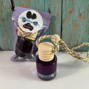 May include: A Golden's Love car air freshener with a purple glass bottle and a wooden cap. The bottle contains a dark purple liquid and is packaged in a clear plastic bag. The bag has a label with the text "Cedar, Musk & Lavender".
