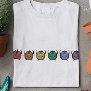 Peut inclure: T-shirt blanc avec une rangée de sept pommes pixelisées arc-en-ciel avec des étoiles jaunes au-dessus de chaque pomme.
