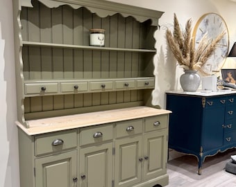 May include: A sage green wooden dresser featuring an open upper shelf with a scalloped trim, five small drawers, a natural wood countertop, and a lower section with four drawers and three cabinet doors, all accented with dark metal hardware.