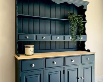 May include: A dark teal dresser with a natural wood worktop, featuring an upper section with open shelving and four small drawers, and a lower section with four drawers and four cabinet doors, all finished with round silver-toned knobs.