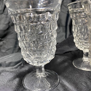 May include: Clear, vintage-style drinking glasses with a diamond pattern. The glasses have a wide rim, a textured body, and a stem with a round base. The glassware is likely made of glass and is suitable for serving beverages.
