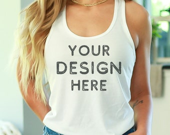 Puede incluir: Un top blanco de tirantes con el texto "YOUR DESIGN HERE" impreso en la parte delantera. El top está siendo usado por una persona con cabello rubio y se combina con pantalones cortos de mezclilla.