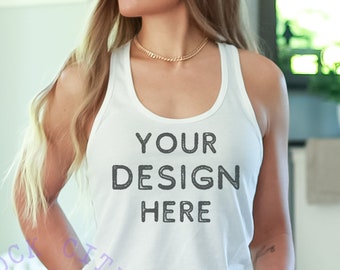 Puede incluir: Camiseta blanca de tirantes con el texto "YOUR DESIGN HERE" impreso en la parte delantera. La camiseta está siendo usada por una persona con el pelo largo y rubio.