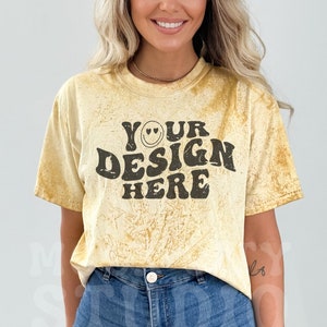Puede incluir: Una camiseta amarilla tie-dye con el texto "YOUR DESIGN HERE" en negro. El texto está en una fuente retro con una carita sonriente.