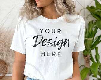 May include: A white t-shirt with the text "YOUR Design HERE" printed on the front. The shirt is being worn by a person with blonde hair and is paired with denim shorts.