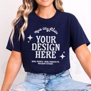 May include: A navy blue t-shirt with the text "Mock City Studio" and "Your Design Here" in white. The text is surrounded by small white stars. The text "Real People - Real Products Mockup Studio" is also in white below the main text.