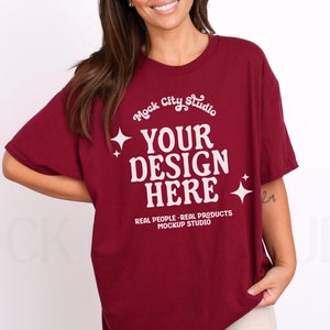 Può includere: Una maglietta oversize color granata con una grafica bianca che dice "Mock City Studio" e "Your Design Here" con stelle e il testo "Real People-Real Products Mockup Studio".