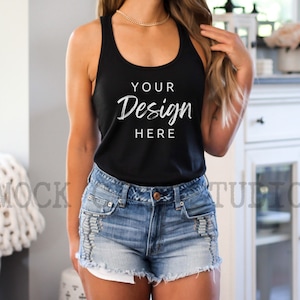 Puede incluir: Un top negro de tirantes con el texto "YOUR Design HERE" impreso en la parte delantera. El top está siendo usado por una persona con cabello largo y castaño y se combina con pantalones cortos de mezclilla.