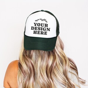 Könnte beinhalten: Grün-weiße Trucker-Mütze mit dem Text "YOUR DESIGN HERE" in fetten schwarzen Buchstaben. Die Mütze hat eine Netzrückseite und einen gebogenen Schirm. Die Person trägt lange, wellige blonde Haare.