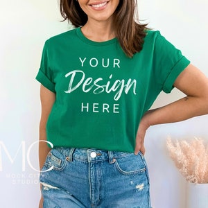 May include: A woman wearing a green t-shirt with the text "YOUR Design HERE" printed on the front. She is wearing blue denim shorts and has her hand on her hip.