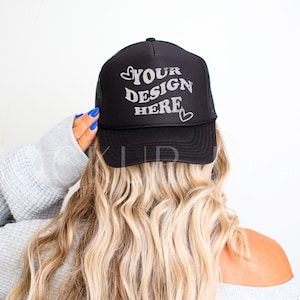 May include: Black trucker hat with a white mesh back. The hat has the text "YOUR DESIGN HERE" in a white, retro font with two small hearts on either side of the text.
