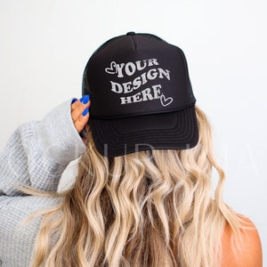 Könnte beinhalten: Schwarze Trucker-Kappe mit weißem Netzrücken. Die Kappe hat ein weißes Design mit der Aufschrift "YOUR DESIGN HERE" und zwei kleinen Herzen auf beiden Seiten des Textes.