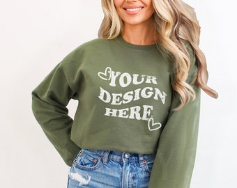 May include: A green sweatshirt with the text "YOUR DESIGN HERE" in white on the front and the same text on the left sleeve. The sweatshirt is being worn by a person with long blonde hair and blue jeans.