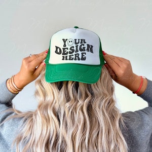 May include: A green and white trucker hat with a mesh back. The front of the hat has the text "YOUR DESIGN HERE" in black with a smiley face.